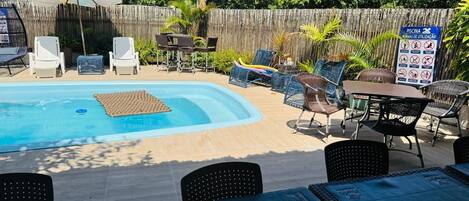 A backyard with a swimming pool, lounge chairs, and a wooden fence.