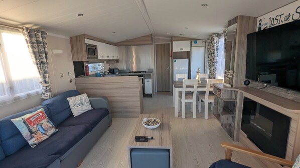 A compact living area with a sofa, a small table, a TV, and a kitchenette. - Lighthouse Lodge Dog Friendly Nr Sutton on Sea (Mablethorpe)