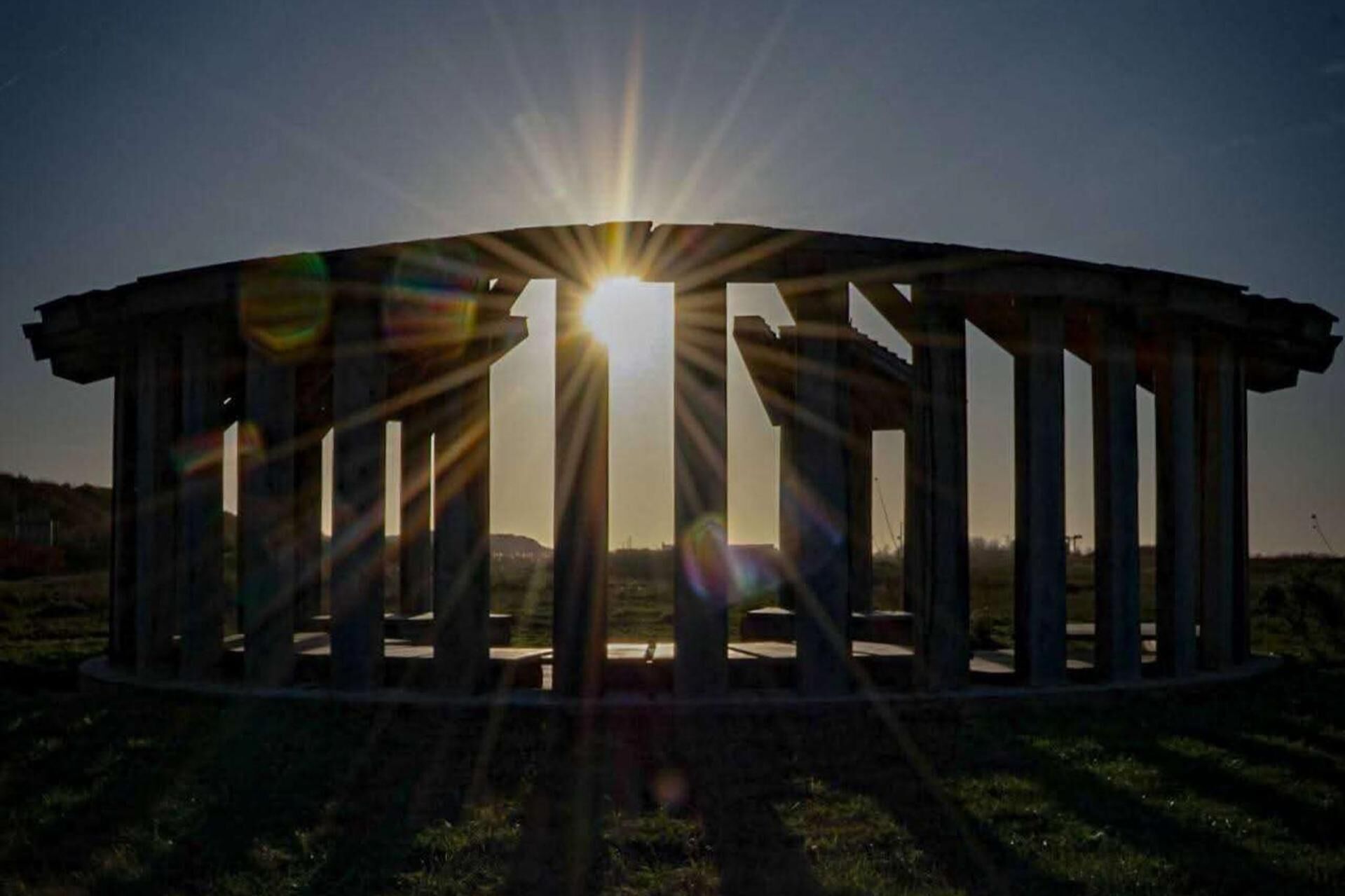 Une structure circulaire soutenue par des colonnes, qui pourrait être un belvédère, sous un ciel dégagé avec le soleil placé juste au-dessus.