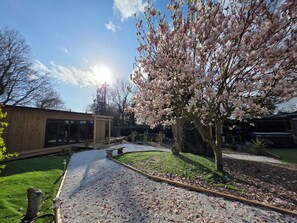 A garden with a wooden structure, a pathway, and a tree with pink blossoms. - Lighthouse Lodge Dog Friendly Nr Sutton on Sea (Mablethorpe)
