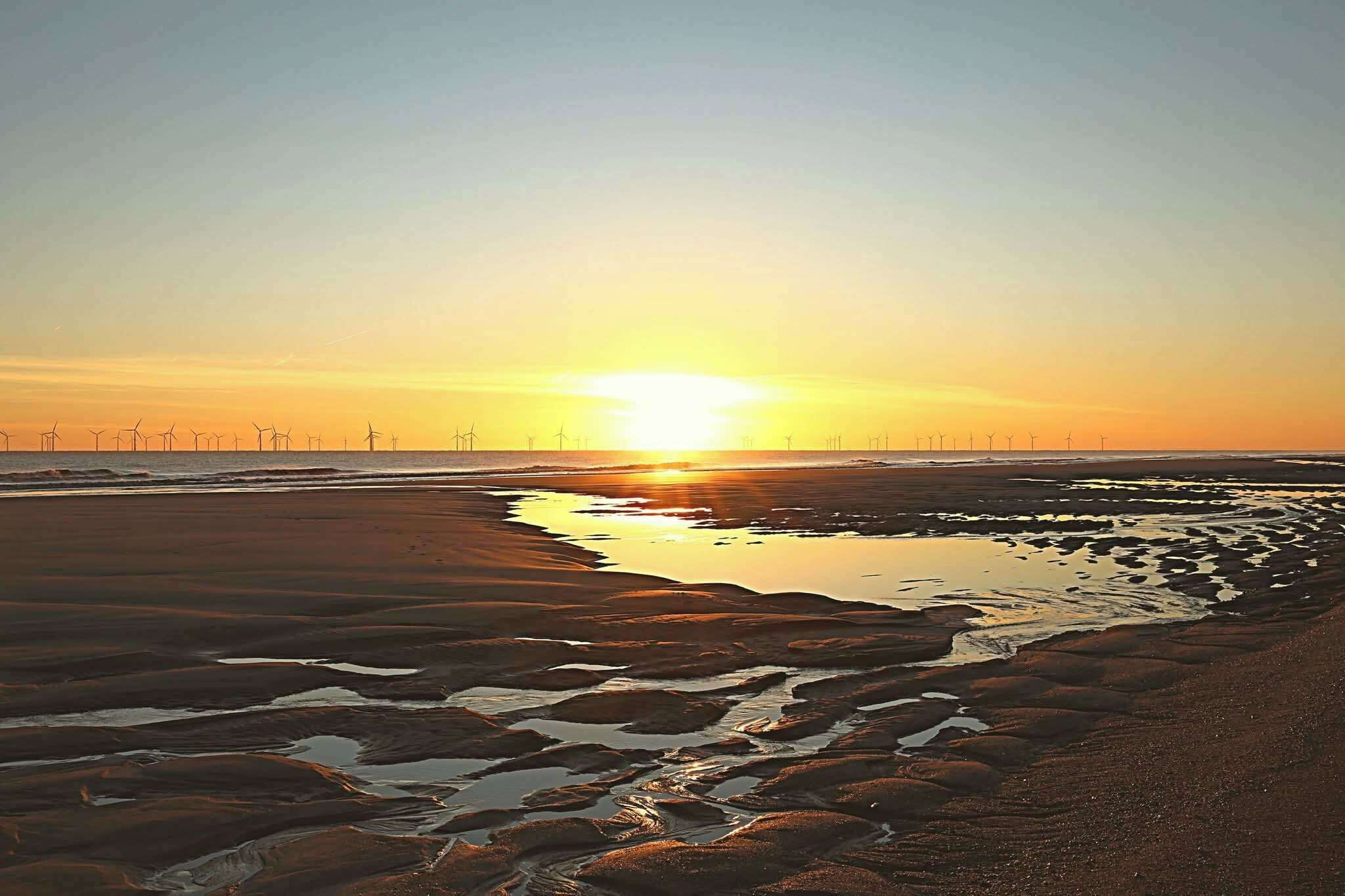 A beach at sunset with wind turbines in the distance.