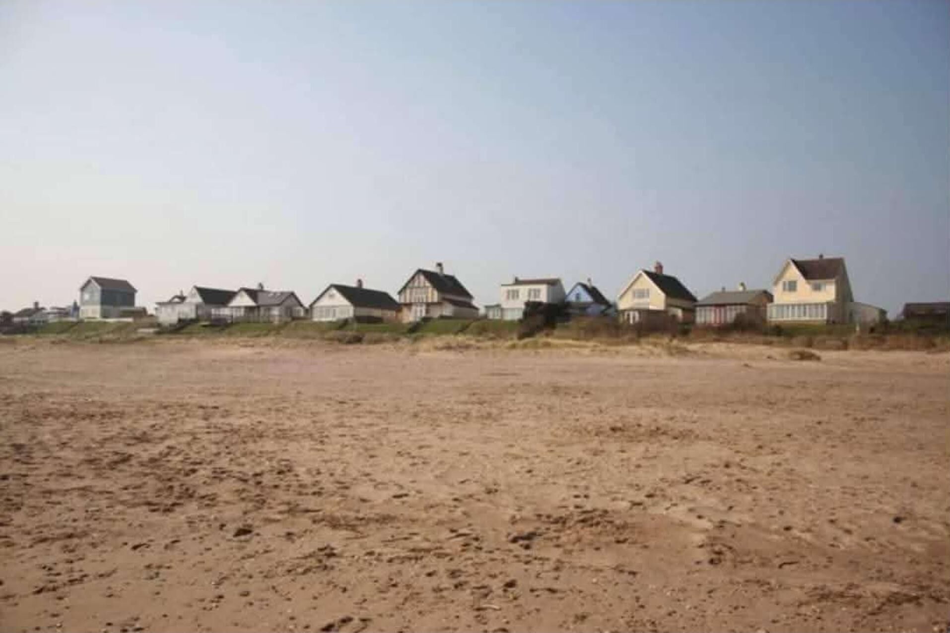 Een rij strandhuisjes met een zandvlakte voor.