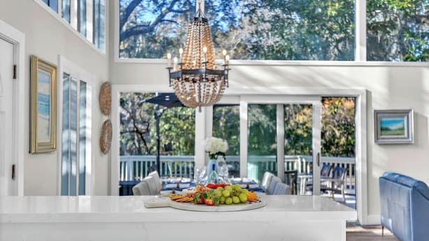 A kitchen with a white countertop, a chandelier, and a dining area with a blue couch. - Gorgeous Coastal Beach Home w/ Pool, Hilton Head (Hilton Head Island)