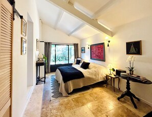 Une chambre à coucher avec un lit, un bureau, une chaise, une fenêtre et un tableau accroché au mur.