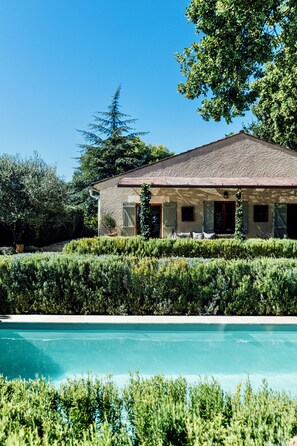 A house with a swimming pool, surrounded by well-maintained hedges and trees.