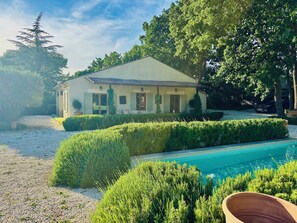Une maison avec une piscine, entourée de haies et d’arbres bien entretenus.