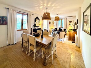 Un coin repas avec une table en bois, quatre chaises et des lampes en osier suspendues au plafond.