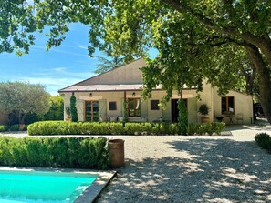 A house with a swimming pool, surrounded by well-maintained hedges and a large tree.