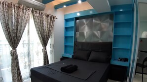 A modern bedroom with a large bed, a headboard with a geometric pattern, and a built-in shelving unit. - City Suites by P&J (Cebu City)