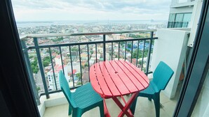 A balcony with a red table and two chairs, overlooking a cityscape with buildings and a bridge. - City Suites by P&J (Cebu City)