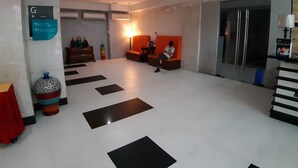 A hotel lobby with a reception desk, a seating area with a person sitting, and directional signs on the wall. - City Suites by P&J (Cebu City)