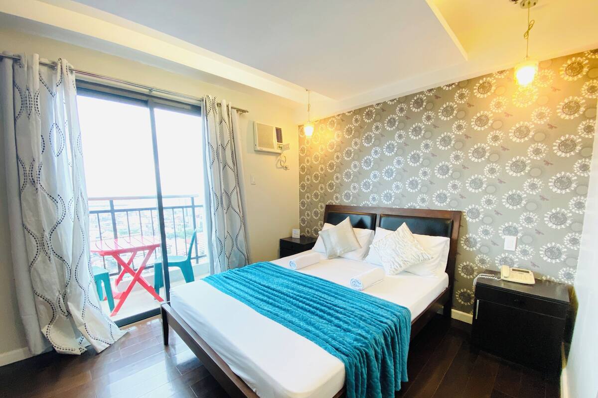 A hotel room with a bed, a nightstand, a telephone, and a view of the outside balcony.