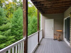 Eine Veranda aus Holz mit weißer Geländer, einer Tür und einem Schaukelstuhl.