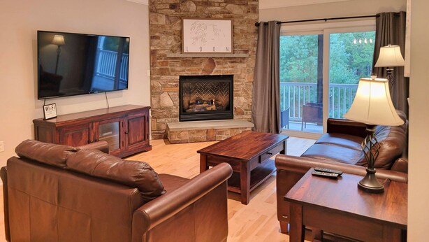 A living room with a stone fireplace, leather sofas, a flat-screen TV, and a balcony with curtains.