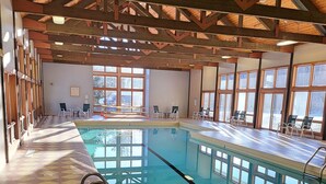An indoor swimming pool with tiled floors, clear water, and wooden beams on the ceiling.