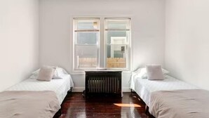 Een kamer met twee bedden, een radiator en een raam met jaloezieën.
