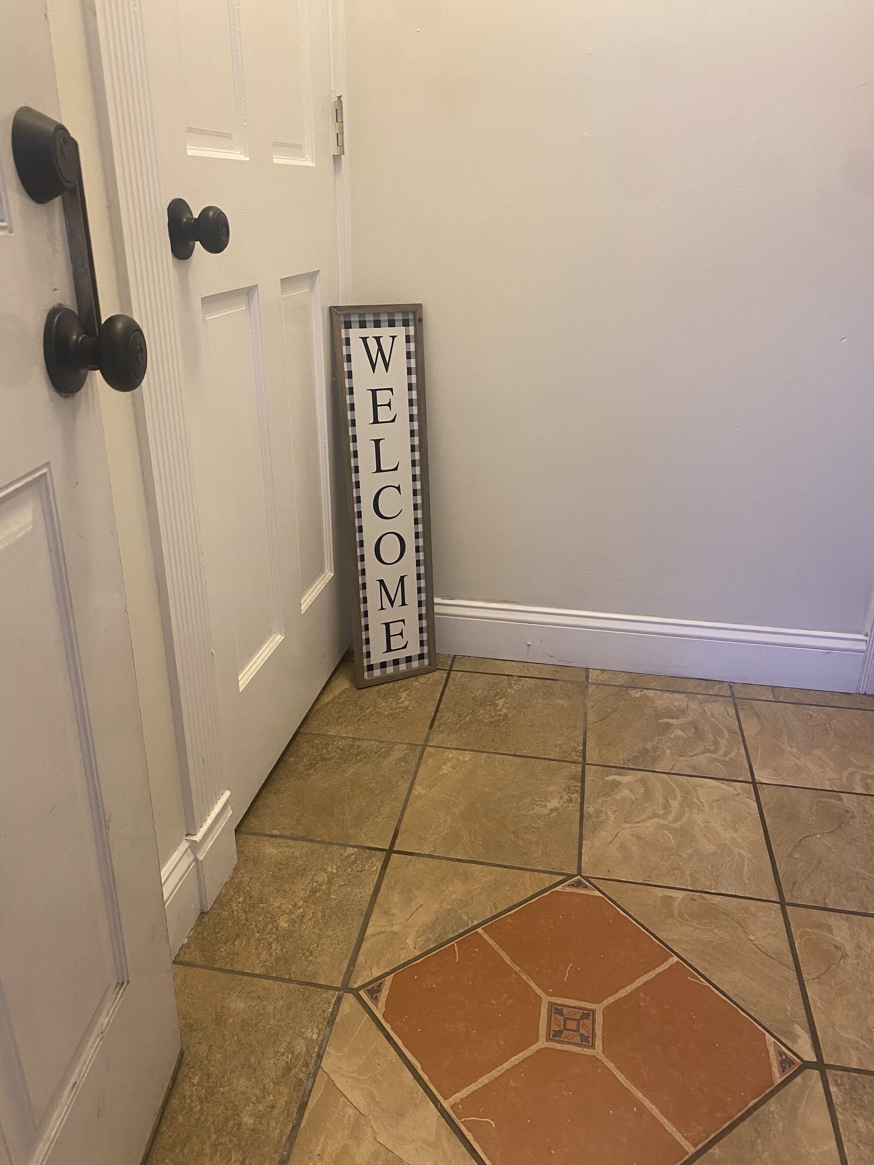 A hallway with a welcome sign, a door with a black handle, and a tiled floor.