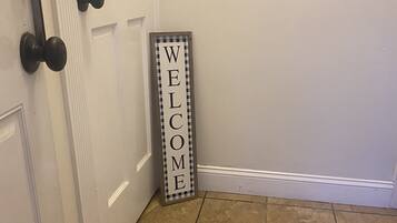 A hallway with a welcome sign, a door with a black handle, and a tiled floor.