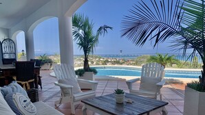 A covered outdoor seating area with white chairs and a sofa, a pool, and a view of the ocean. - 400 m2 dream villa / 180 degree panoramic sea view, in top location!  (Dénia)