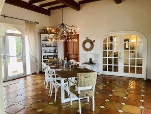 A dining area with a wooden table set for six, surrounded by white chairs, a chandelier, and a view through a glass door. - 400 m2 dream villa / 180 degree panoramic sea view, in top location! (Dénia)