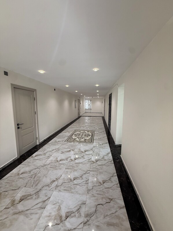 A long, narrow hallway with white walls and a marble floor, leading to a door at the end. - Yasamal Hostel (Baku)