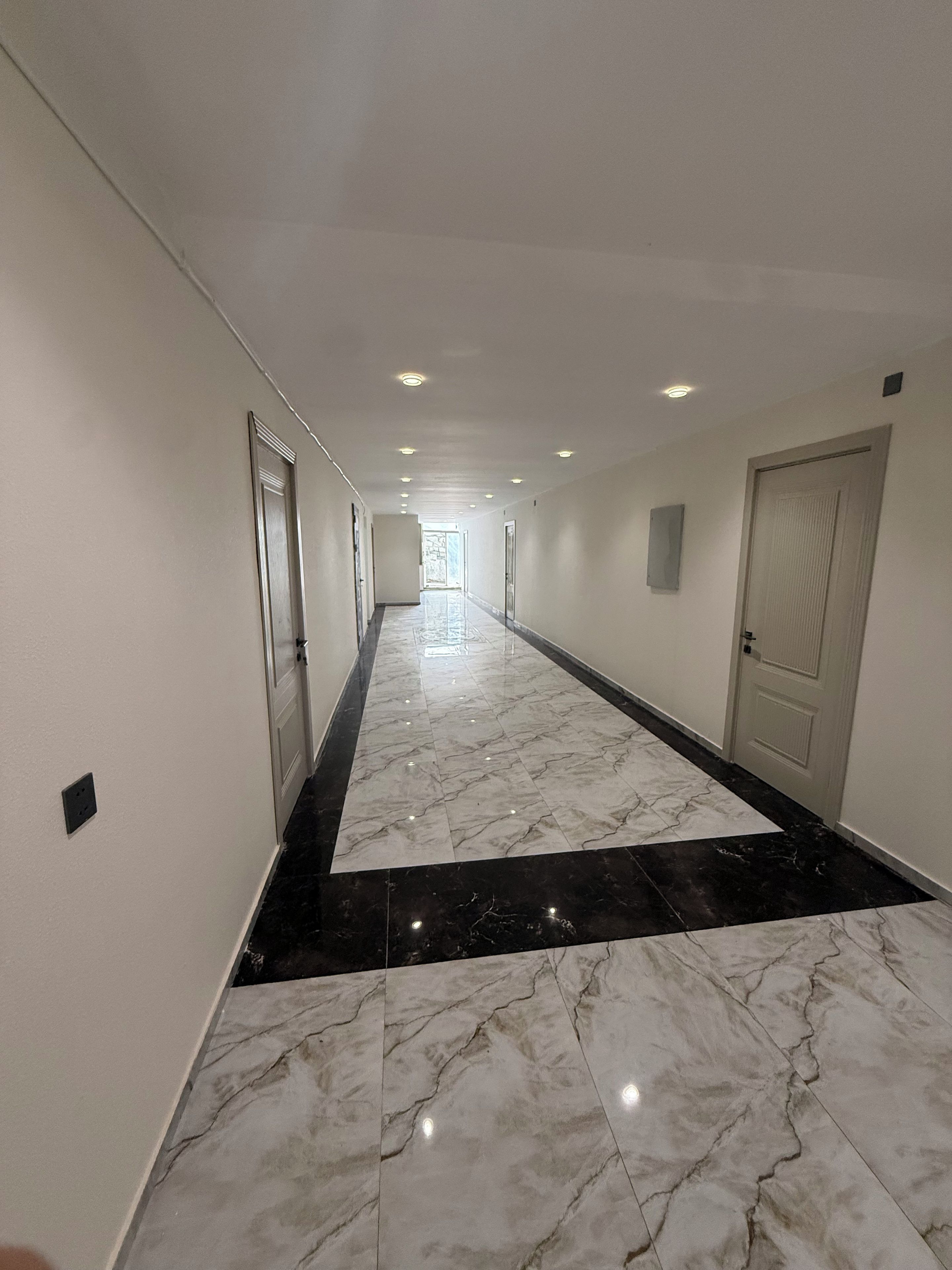 A hotel corridor with a marble floor, doors on both sides, and recessed lighting.