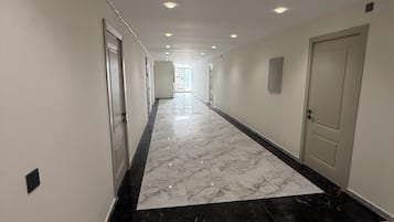 A hotel corridor with a marble floor, doors on both sides, and recessed lighting.