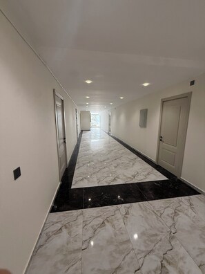 A hotel corridor with a marble floor, doors on both sides, and recessed lighting. - Yasamal Hostel (Baku)