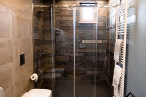 A modern bathroom with a glass-enclosed shower, stone walls, a toilet, and a towel rack. - Casa Vittoria, a charming vacation home just 5 minutes from the beach. (Monopoli)