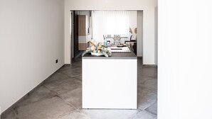 Een moderne keuken met een centraal eiland, een eethoek met een tafel en stoelen, en uitzicht op een kamer met een raam.