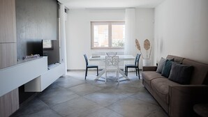 Een moderne woonkamer met een bank, een eettafel met stoelen, een tv op een dressoir en een raam met gordijnen.