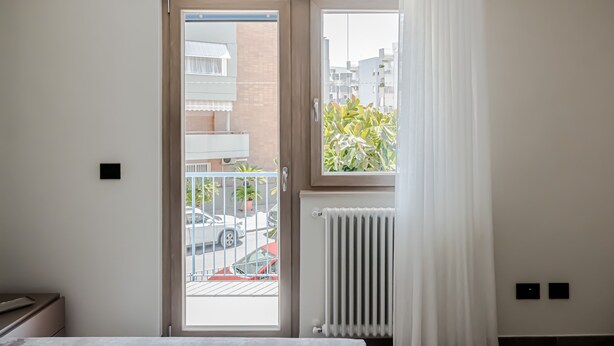Een kamer met een bed, een radiator, een raam met uitzicht op de straat, en een deur.