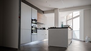 Een moderne keuken met witte kasten, een centraal eiland en een groot raam dat natuurlijk licht binnenlaat.