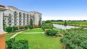 Een meerlaags hotel met balkons, een verzorgd gazon en uitzicht op een rivier.