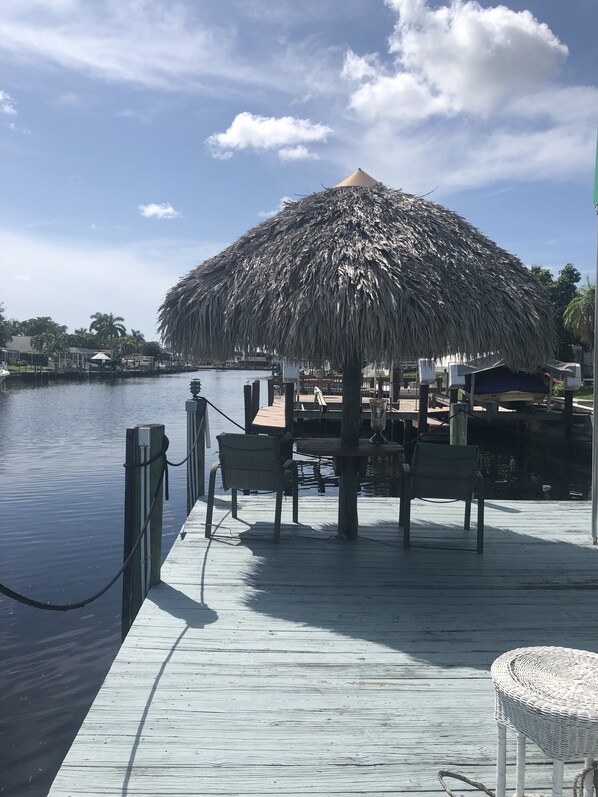 A wooden dock with a thatched umbrella, wooden chairs, and a table with a vase. - Villa Caribbean Spirit, Cape Coral, Florida (Cape Coral)