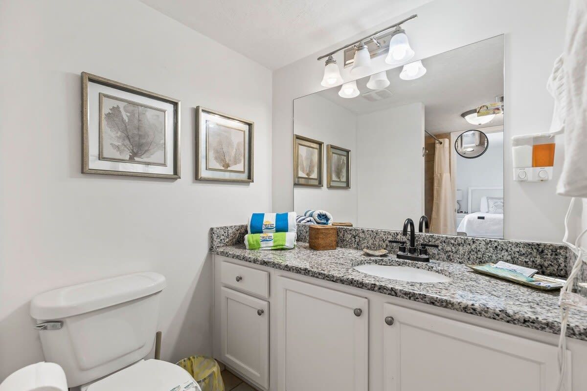 A bathroom with a white toilet, a granite countertop sink, and a mirror above.