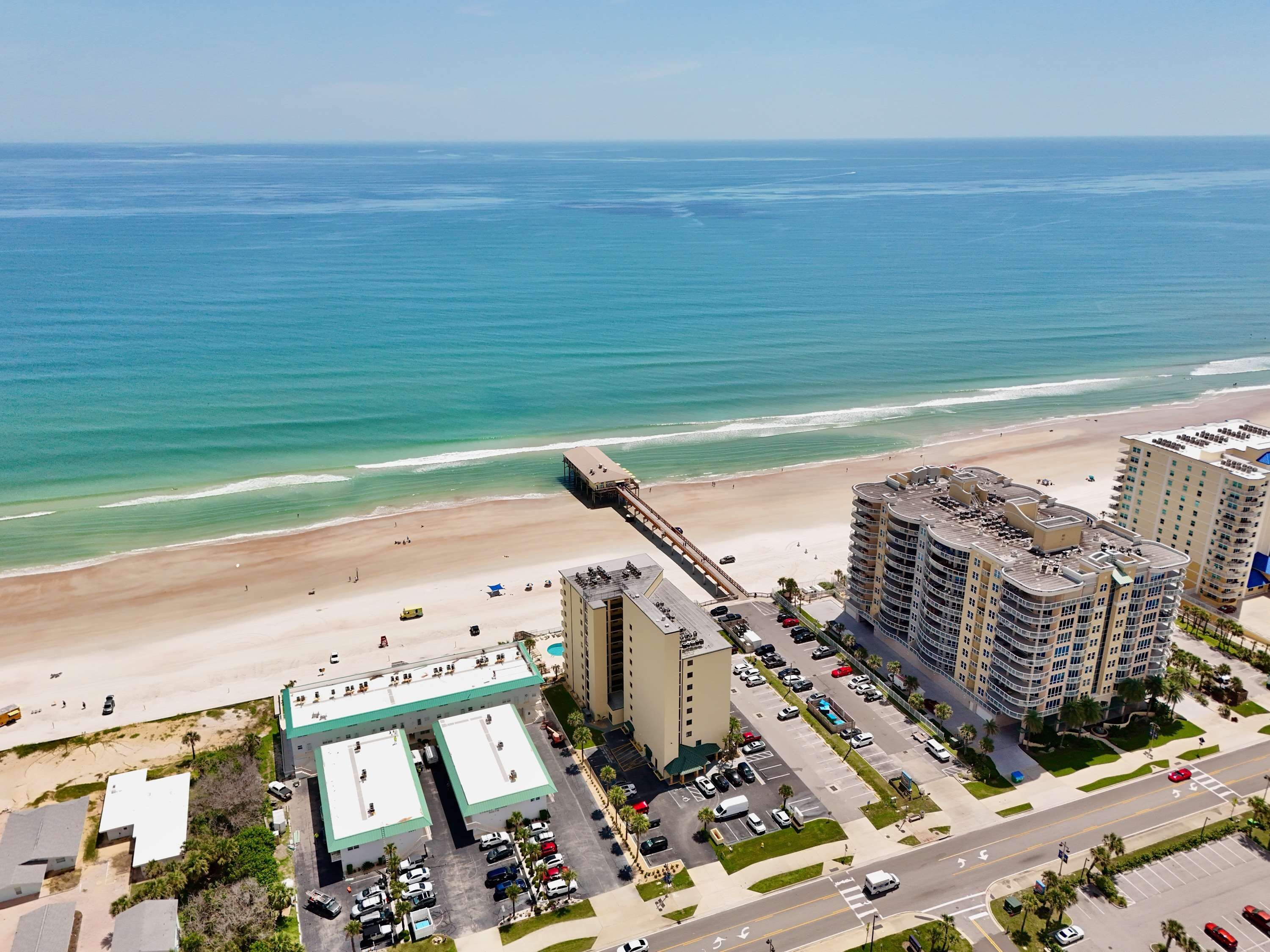 Un hotel sul lungomare con vista sulla spiaggia, parcheggio e un ponte pedonale.