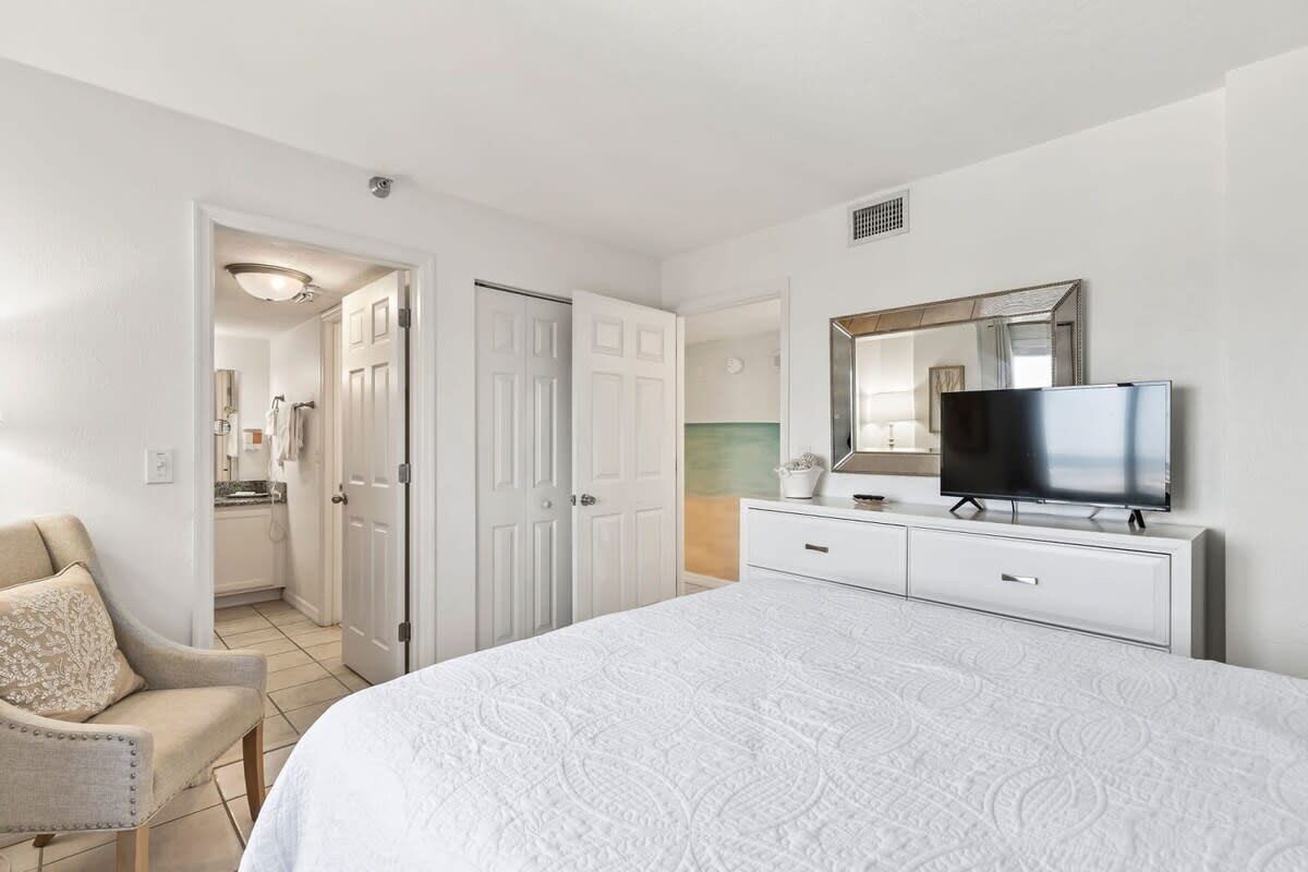 Une chambre avec un grand lit, un téléviseur posé sur une commode et une porte donnant sur une salle de bain.