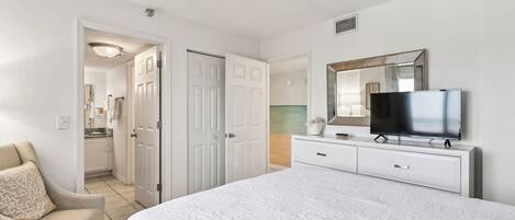 Une chambre avec un grand lit, un téléviseur posé sur une commode et une porte donnant sur une salle de bain.