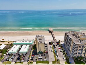 A coastal hotel with a parking lot, a beach, and a pier.