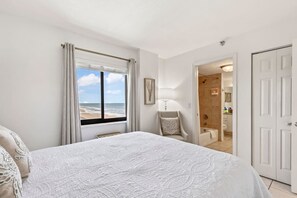 A bedroom with a large bed, a view of the beach, a bathroom, and a door. - Top Floor Oceanfront Condo w/ Pool & Beach Access! (Daytona Beach Shores)