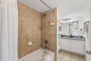 A bathroom with beige tiles, a bathtub, a shower, a toilet, and a sink with a mirror. - Top Floor Oceanfront Condo w/ Pool & Beach Access! (Daytona Beach Shores)
