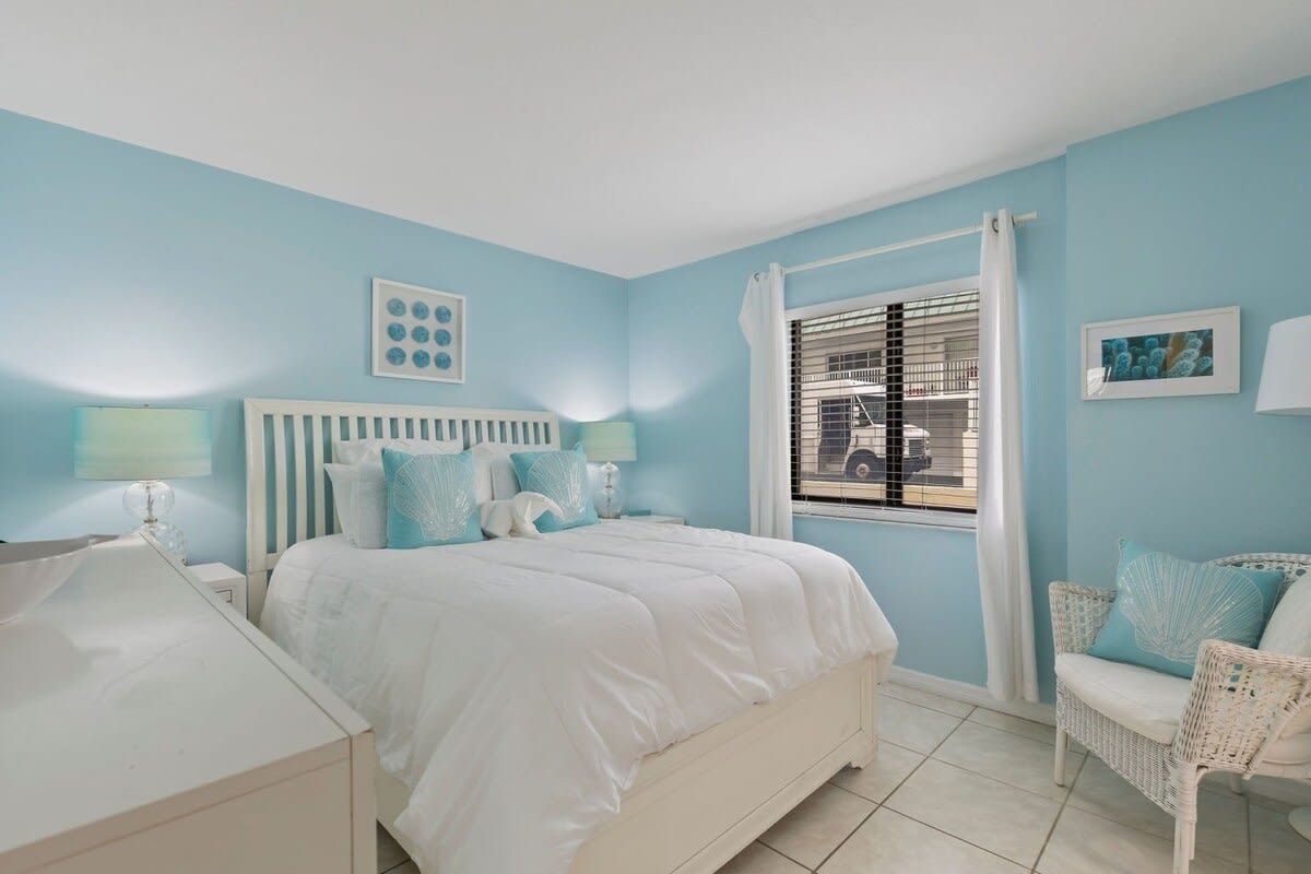Une chambre à coucher avec un lit, des tables de chevet, une chaise et une fenêtre avec des stores.