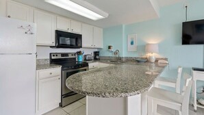 A kitchen with white cabinets, a granite countertop, a microwave, a stove, and a sink. - Poolside Suite 101 | Beach Front, Pool & Hot Tub (Daytona Beach Shores)