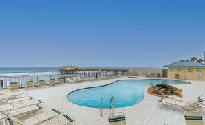 A pool area with lounge chairs and a view of the beach.