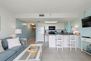 A compact living space with a kitchenette, a sofa, a coffee table, and a TV mounted on the wall.