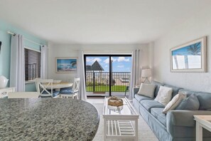 A modern living room with a dining table, a sofa, and a view of a balcony with a pool. - Poolside Suite 101 | Beach Front, Pool & Hot Tub (Daytona Beach Shores)
