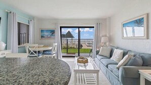 A modern living room with a dining table, a sofa, and a view of a balcony with a pool. - Poolside Suite 101 | Beach Front, Pool & Hot Tub (Daytona Beach Shores)