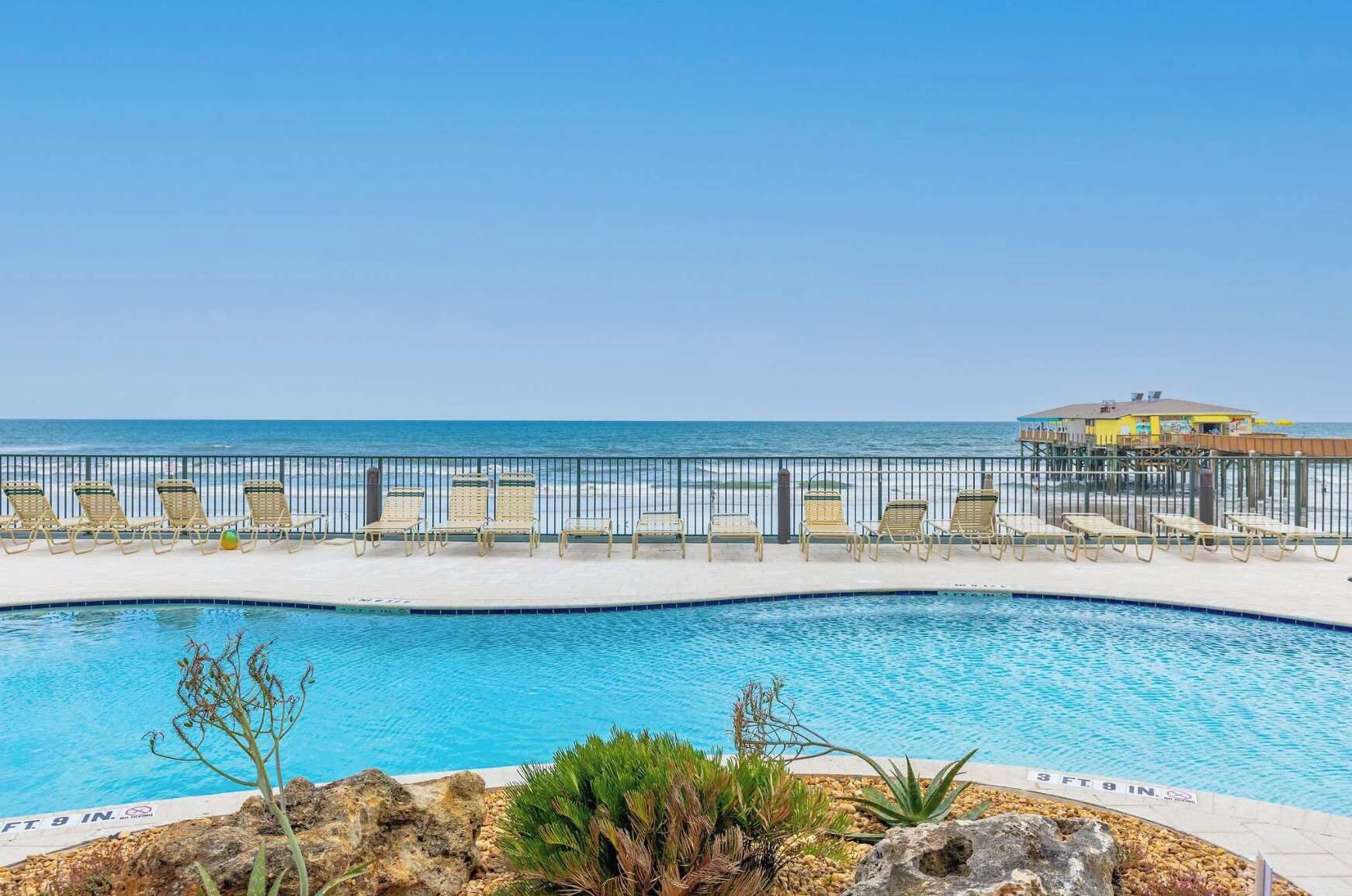 Ein Pool mit Blick auf den Ozean, umgeben von Liegestühlen und einem Zaun.
