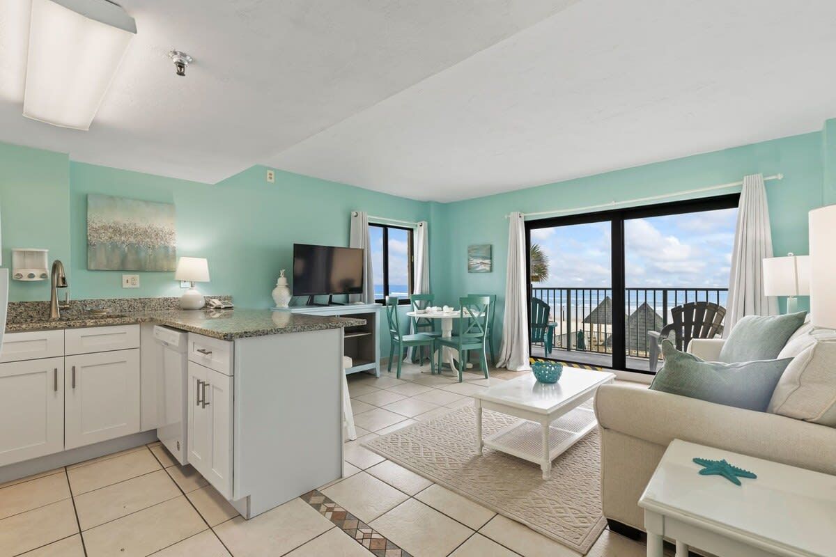 A modern living room with a kitchen, a dining area, and a balcony with a view.